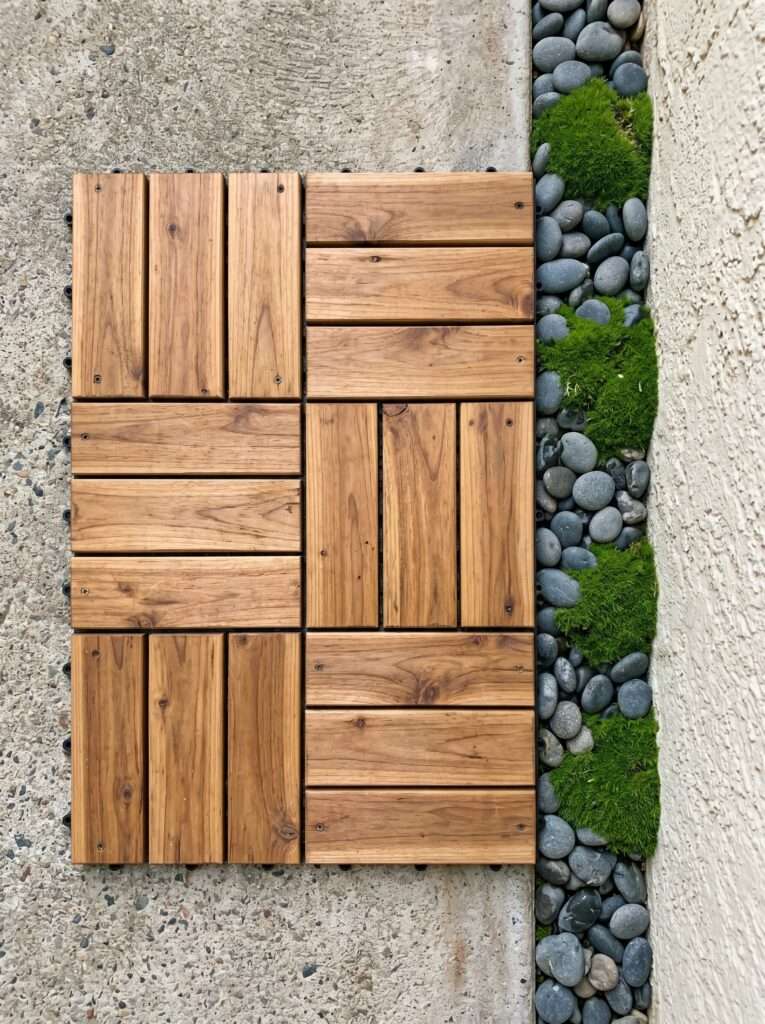 Interlocking cedar deck tiles edged with river stones and green moss.