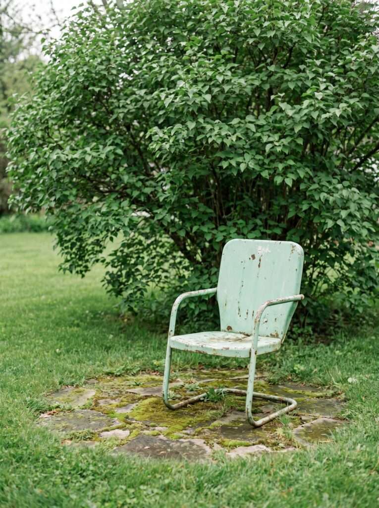 Vintage mint green metal spring chair on a small flagstone pad tucked behind lilacs.
