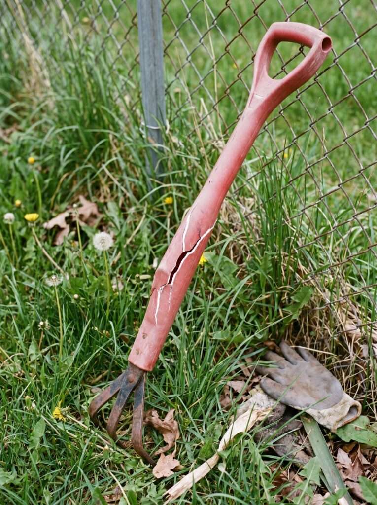 Broken stand up claw weeding tool lying discarded in tall grass