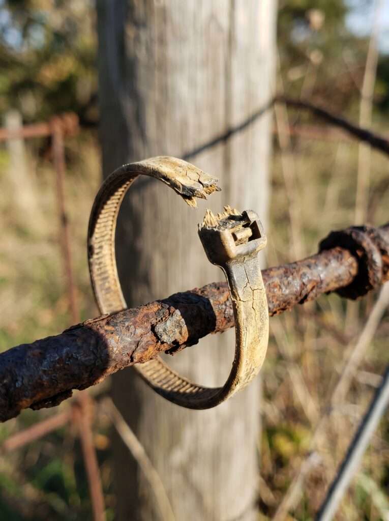 A weathered, snapped plastic tie on an old outdoor wire structure.