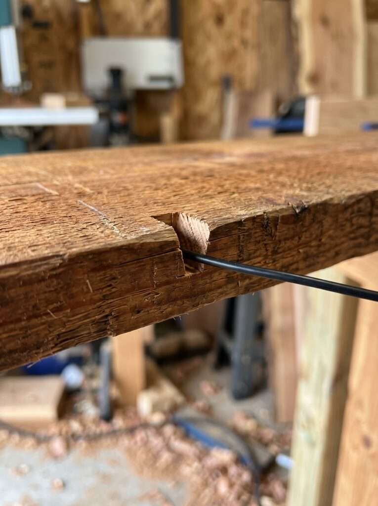 A small wire relief notch cut into the wooden top cap of a garden water feature.