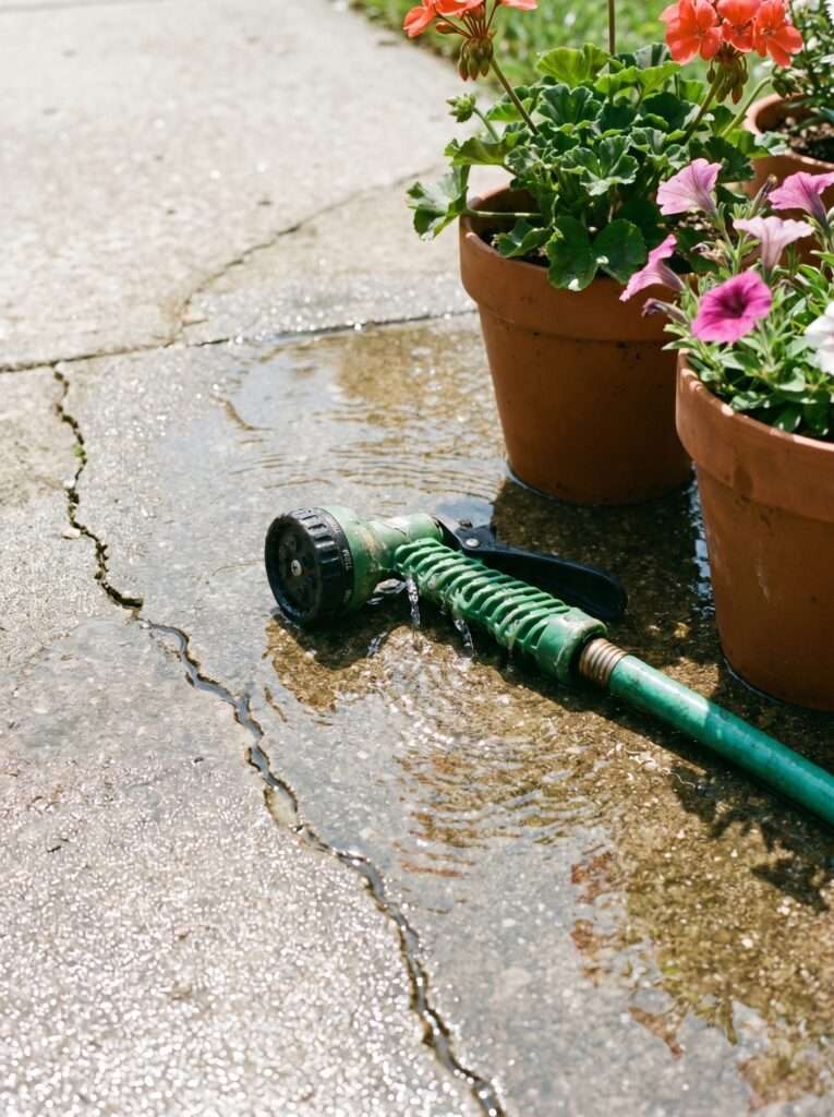 Leaking plastic garden hose nozzle dropping water on concrete driveway