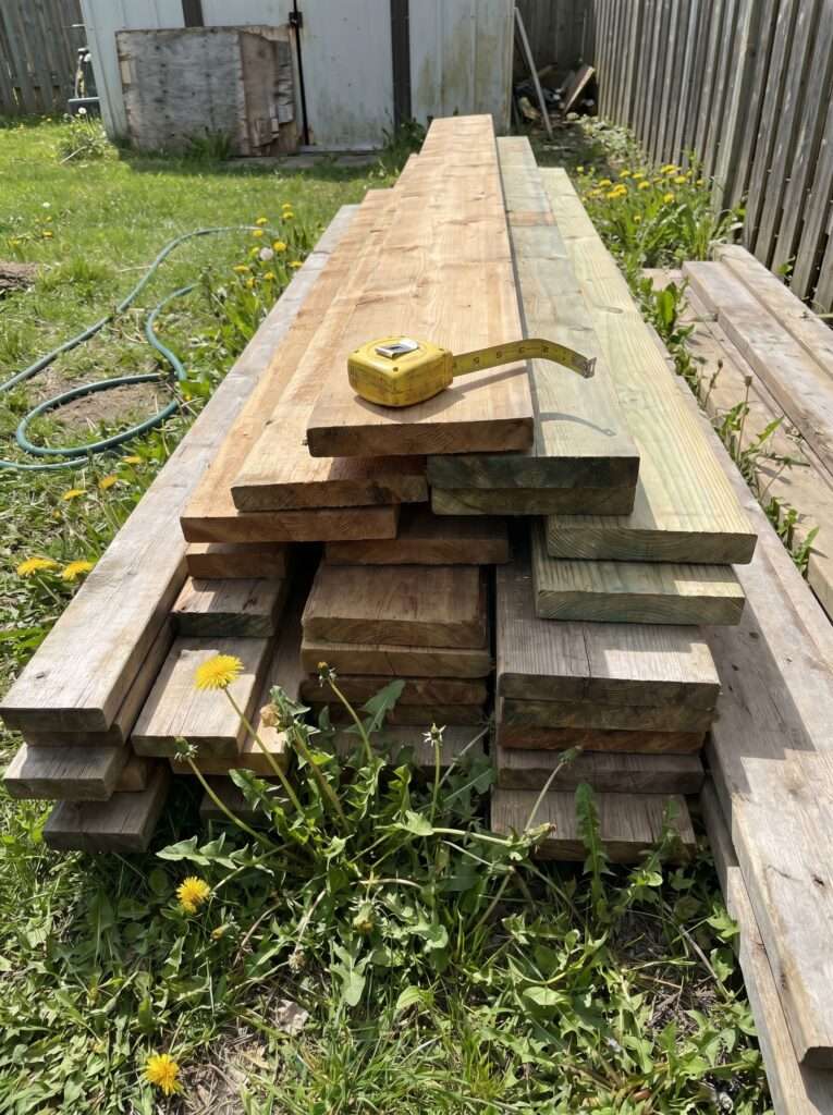 Stacked cedar lumber and pressure-treated boards ready for a backyard DIY project on a real lawn.