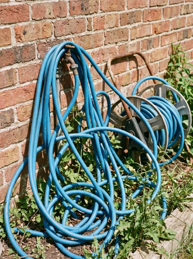 Tangled and kinked blue coiled garden hose against a brick wall
