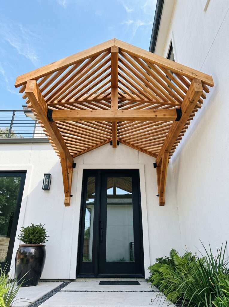 Wood pergola accent awning with chevron pattern shade slats over a black exterior door.
