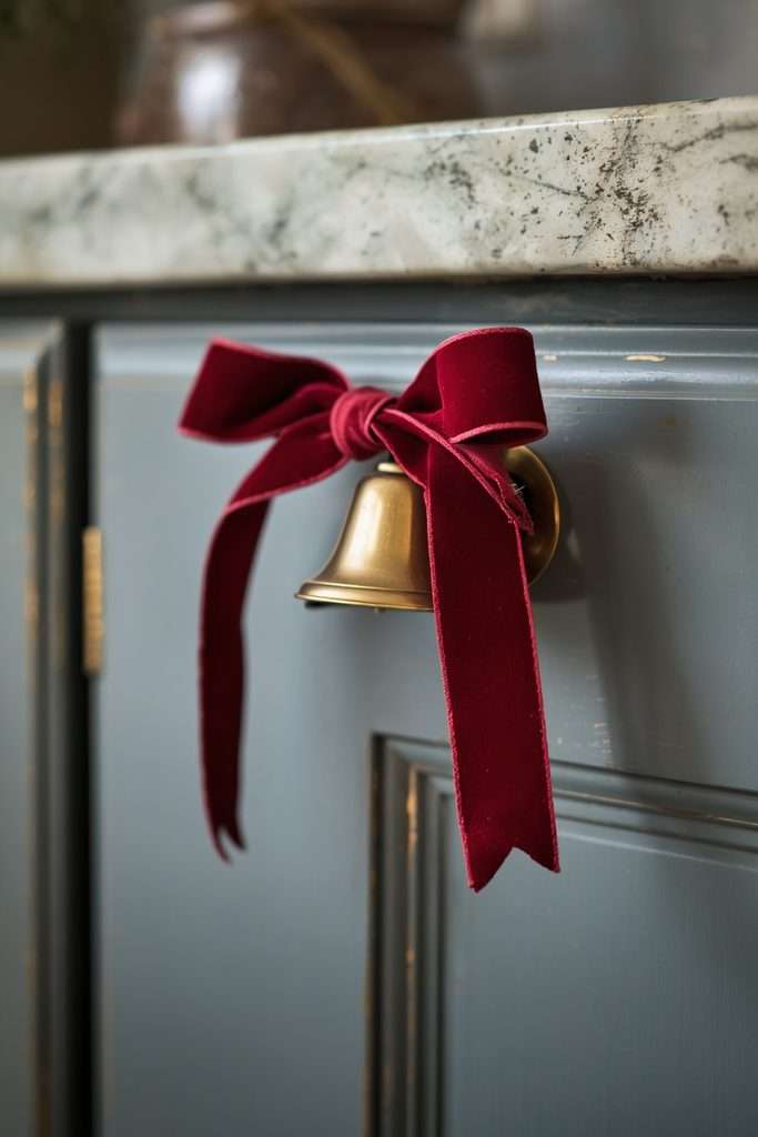 Brass Christmas bell tied with velvet ribbon on a kitchen cabinet.