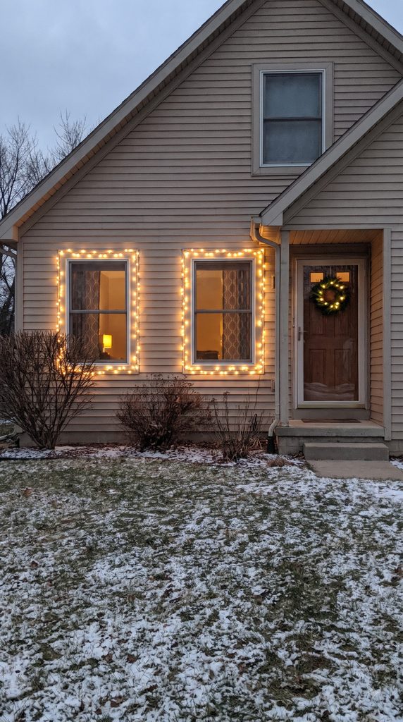 Small solar pathway lights illuminate a garden walkway leading to a Christmas-decorated front porch at dusk.