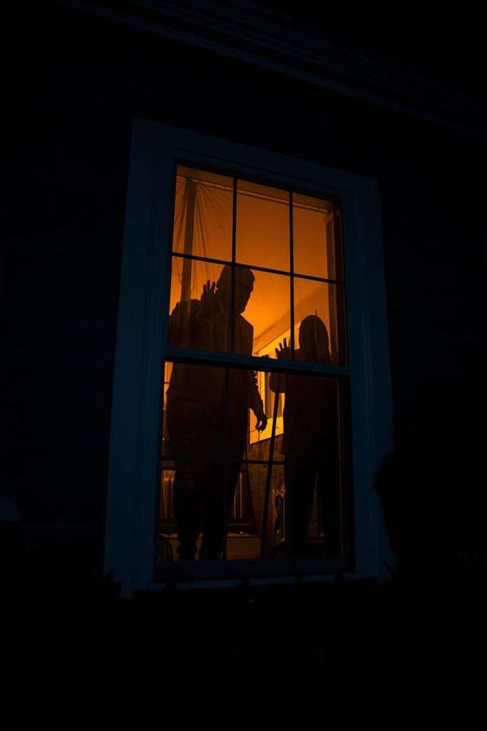 Creepy Halloween silhouettes visible through a suburban house window.