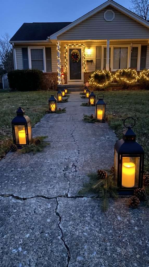 Black metal Christmas lanterns with warm glowing candles line a walkway leading to a decorated front porch.