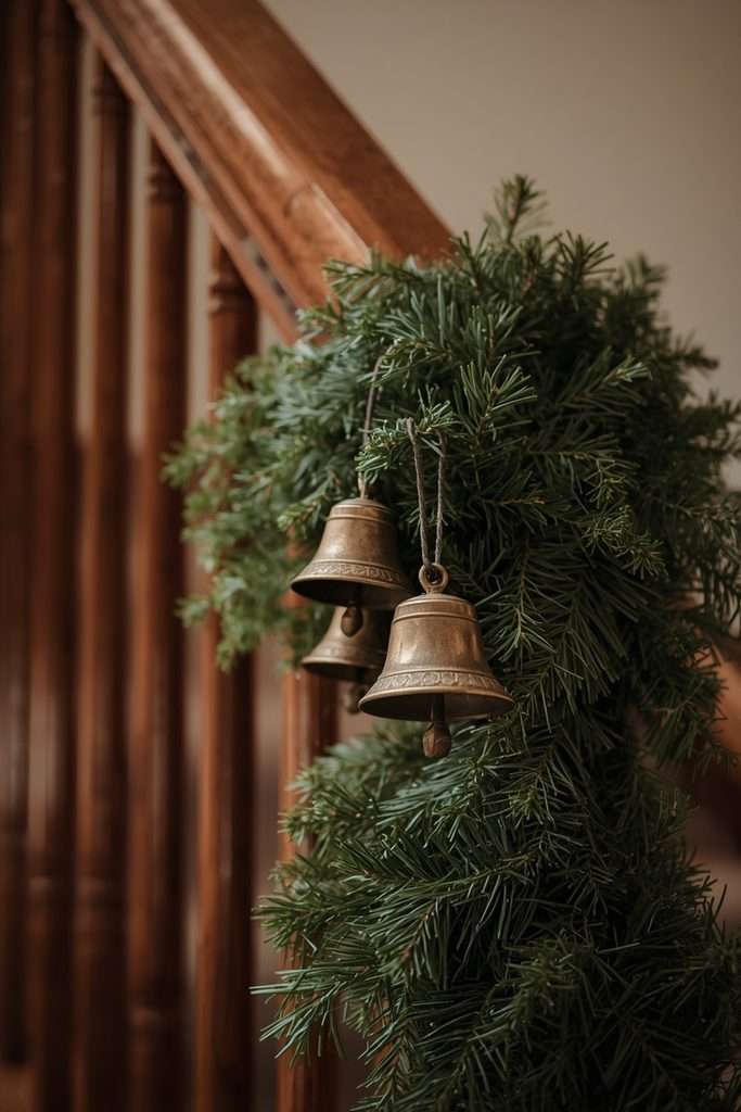 Aged brass bells arranged along an evergreen Christmas staircase garland.